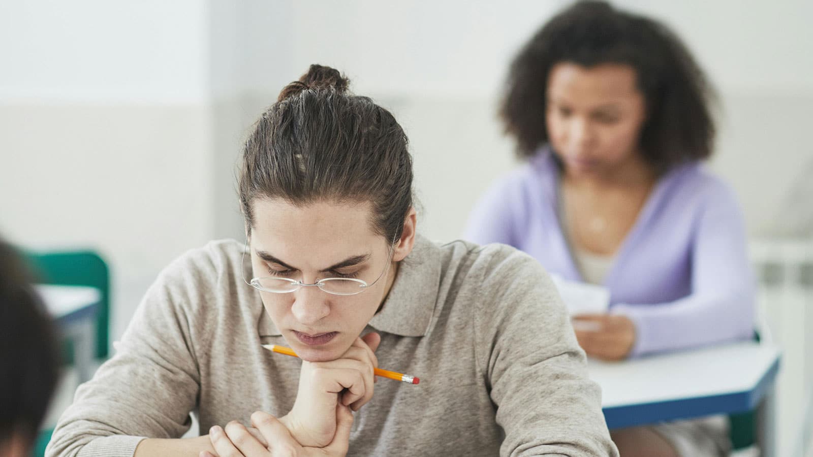 Two students sitting at a desk looking down at their papers while taking a test