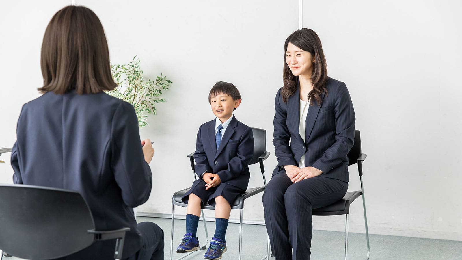 Mother and child dressed up sitting in chairs in front of a woman interviewing them